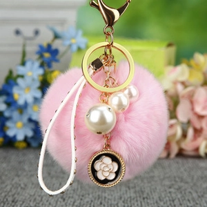 Gros plan d'un porte-clés pompon rose avec fleur de camélia blanc et métal doré
