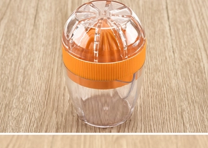 Macro detail of a compact orange and clear citrus juicer on a light wood background