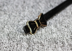 Détail d'une ceinture fine en cuir verni noir avec boucle nœud en émail doré élégante