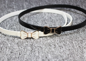 Détail de ceintures fines en cuir verni avec boucles en métal nœud noires et blanches