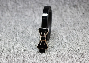 Détail d'une ceinture en cuir verni noir avec une boucle en forme de nœud doré