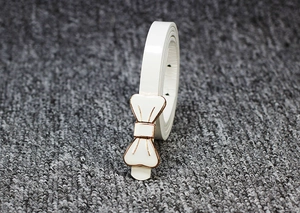 Détail d'une ceinture fine en cuir verni blanc avec boucle nœud dorée pour robes