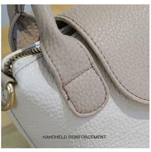 Macro-opname van versterkte stiksels en litchi-nerfleertextuur op een beige handtas