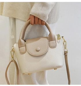 Detail van de beige kiezellederen handtas met gebogen handvat en gouden metalen studs