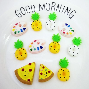 Flat lay of resin pineapple and pizza charms on a white ceramic plate for DIY crafts