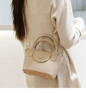 Detail van beige mini-tas van generfd leer met gouden hardware en beschermende pootjes