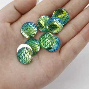 Close-up of 16mm green iridescent fish scale resin cabochons held in hand for DIY jewelry
