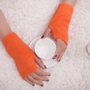 Detail of warm orange knitted fingerless gloves held over a white plush background