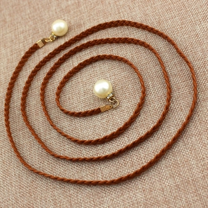 Brown woven waist chain belt with pearl pendants on beige linen background