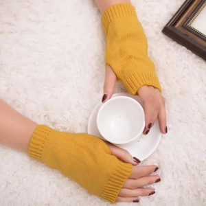 Detail of ginger knit fingerless gloves holding a white mug on a plush white carpet