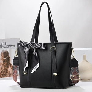 Close-up of black leather bucket bag featuring a colorful wide strap and silk scarf detail
