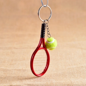 Detail of a mini tennis racket and ball keychain with a red frame on a burlap background