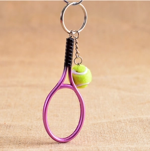 Detailed close-up of a pink tennis racket and yellow ball keychain on brown linen background