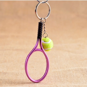 Detailed view of a purple metal tennis racket and green ball keychain on linen texture