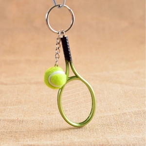 Close-up of a green tennis racket keychain with a yellow mini ball on a rustic background