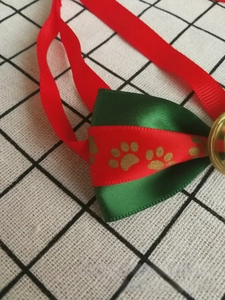 Dettaglio del papillon festivo per cani con stampa di zampe dorate e campanellino in metallo