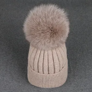 Close-up of warm beige knit beanie featuring thick ribbing and a large faux fur pompom