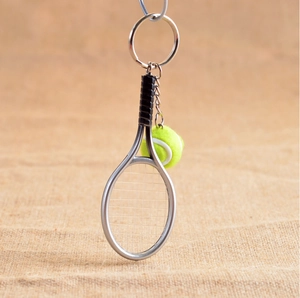 Macro shot of silver metal tennis racket and green felt ball keychain with metal chain