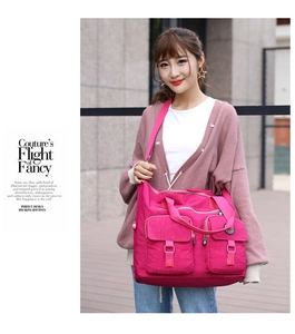 Detail view of pink multi-pocket nylon travel bag with silver buckles shown in a street style