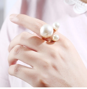 Close-up of golden ring featuring three gradient-sized white pearls on a model's finger