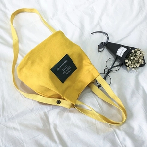 Bright yellow canvas bucket shoulder bag with black woven label on a white background