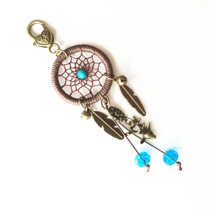 Detail of handmade dreamcatcher keychain with brown weaving, turquoise bead and bronze feathers