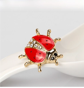 Detail of red enamel ladybug brooch with sparkling rhinestones on a white porcelain spoon