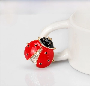 Close-up of a red ladybug brooch with crystals on a white ceramic cup handle