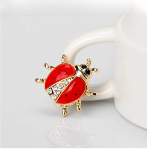 Close-up of ladybug brooch with red enamel and white rhinestones on golden alloy base