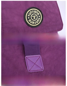 Detail of purple nylon travel bag showing round rubber logo and reinforced cross stitching
