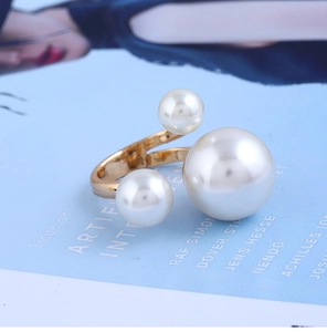 Close-up of golden open ring featuring three white pearls on a fashion magazine