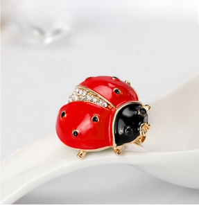 Detailed view of ladybug brooch with red enamel, gold alloy frame and sparkling rhinestones