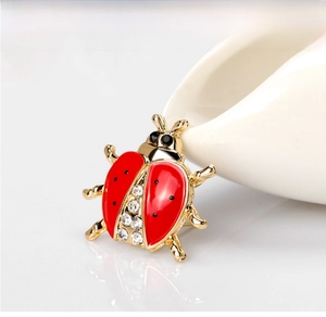 Macro shot of cartoon ladybug brooch with red enamel, gold alloy, and sparkling zircon gems