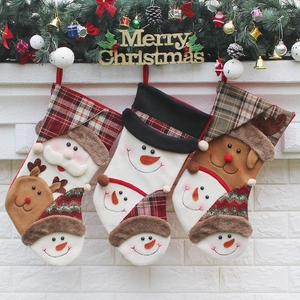 Set di 3 calze natalizie con Babbo Natale e renna appese su una parete di mattoni bianchi