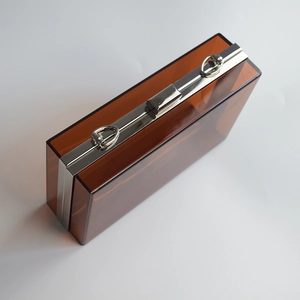 Detail of amber acrylic evening clutch bag with shiny silver metal frame and snap closure
