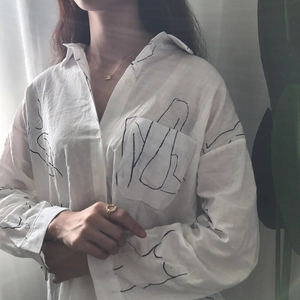 Detail of artistic black line patterns on a white long-sleeved button-down shirt for women