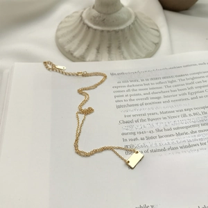 Close-up of a minimalist gold square pendant necklace on an artistic book page background