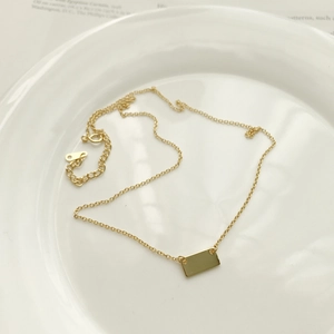 Detailed macro view of a gold square pendant necklace on a decorative ceramic tray
