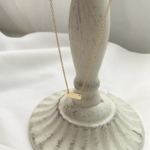 Detail shot of a minimalist gold rectangular bar pendant on a delicate chain necklace