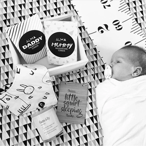 Detail view of baby gift set with milestone cards, bib, and candle on geometric canvas