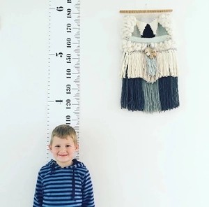 Detail of canvas height chart with wooden bar featuring cm and feet scales on white wall