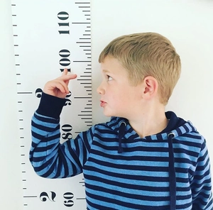Boy measuring height with a cartoon canvas wall hanging growth chart in a modern nursery