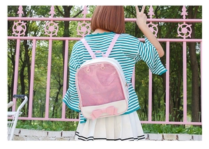 Pink and white ita bag backpack with a clear window and bow detail worn by a model outdoors