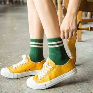 Green cotton crew socks with white double stripes on a concrete and wooden background