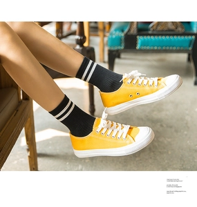 On-foot view of yellow low-top canvas sneakers with white laces in a vintage cafe