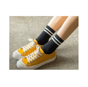 Detail of black cotton mid-calf socks with white stripes paired with yellow canvas sneakers