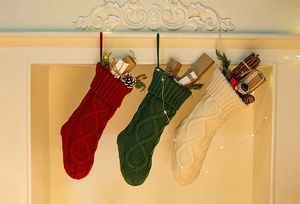 Close-up of knit Christmas stockings in red, green, and white on a festive fireplace mantel