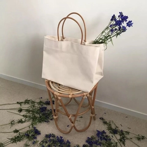 Minimalist cream canvas tote bag with round brown handles on a woven stool