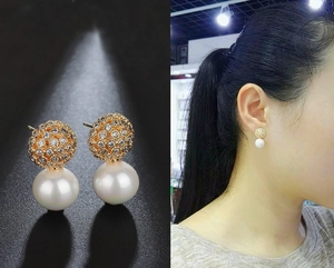 Macro view showing a golden rhinestone ball and white pearl stud earring on model