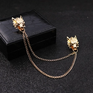 Detail of golden wolf head brooch with long metal chains on a black textured surface